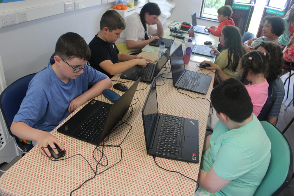 Kids sitting down working on Scratch projects on a laptop each