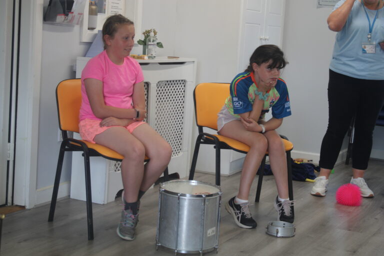 Two Young persons sitting down with a drum on the floor by their feet