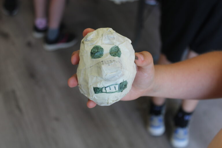 The head of a puppet with a big nose and a big smille being currently made by one of the young people