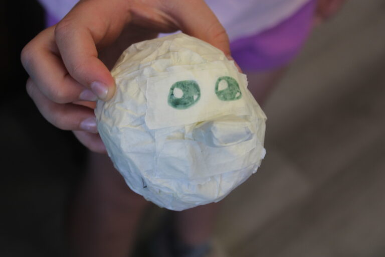 The head of a puppet with a big nose being currently made by one of the young people